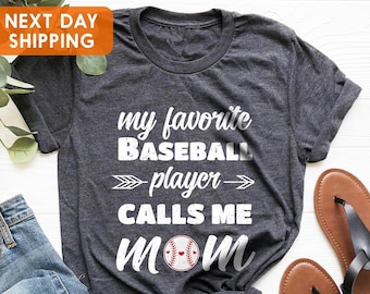 May include: Gray t-shirt with white text that reads "my favorite baseball player calls me mom" with a red baseball and heart graphic.