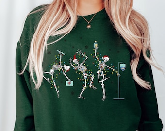 May include: A green sweatshirt with a festive design featuring three skeletons dressed in Santa hats and Christmas lights. The skeletons are holding drinks and a first aid kit.