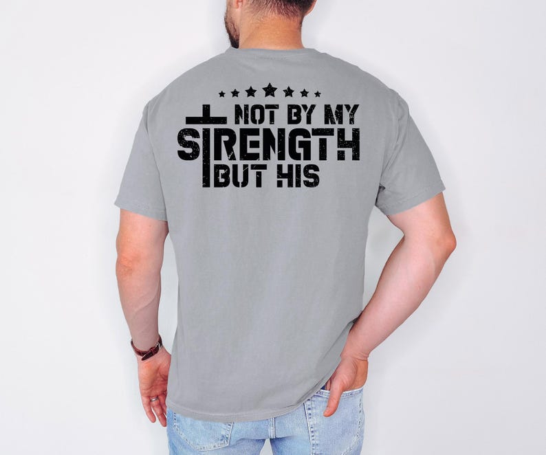 May include: A gray t-shirt with a black graphic that reads "Not by my strength but his" with a cross and stars.