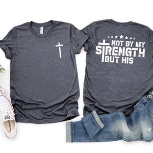 May include: Two heather gray t-shirts with a white cross on the left side and the text "NOT BY MY STRENGTH BUT HIS" on the right side.
