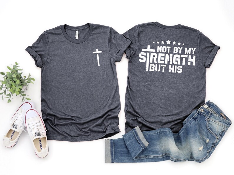 May include: Two heather gray t-shirts with a white cross on the left side and the text "NOT BY MY STRENGTH BUT HIS" on the right side.