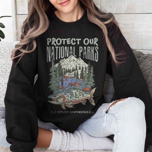 May include: Black sweatshirt with the text "PROTECT OUR NATIONAL PARKS" above a graphic of a mountain, trees, river, and fish. The words "EXPLORE RESPONSIBLY" are below the graphic.