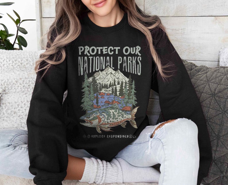 May include: Black sweatshirt with the text "PROTECT OUR NATIONAL PARKS" above a graphic of a mountain, trees, river, and fish. The words "EXPLORE RESPONSIBLY" are below the graphic.