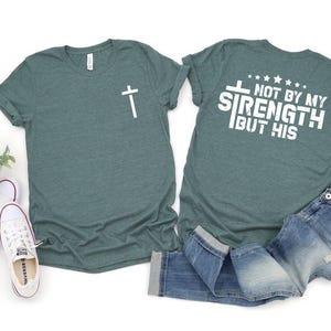 May include: A teal green t-shirt with a cross on the front and the text "Not by my strength but his" on the back.