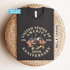 May include: Dark gray t-shirt featuring an eagle, American flags, and the text "United States of America 250th Anniversary 1776-2026". The shirt is made of a soft material and is perfect for celebrating the nation's history.