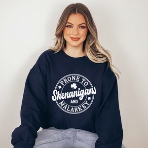 May include: A navy blue sweatshirt with a white circle graphic that says "Prone to Shenanigans and Malarkey" with a shamrock design.