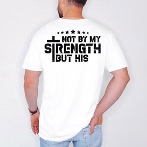 May include: White t-shirt with a black graphic that reads "I Not By My Strength But His" with five stars above the text.
