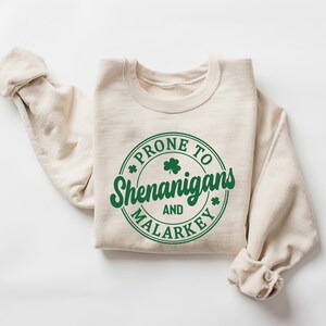 May include: A beige sweatshirt with a green circle graphic that says "Prone to Shenanigans and Malarkey" with a shamrock inside the circle.