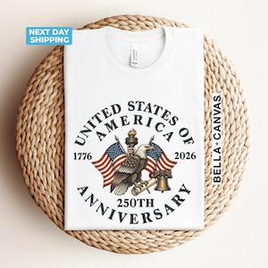 May include: White t-shirt featuring a patriotic design for the 250th anniversary of the United States of America. The design includes an eagle, American flags, and the text "United States of America 250th Anniversary".