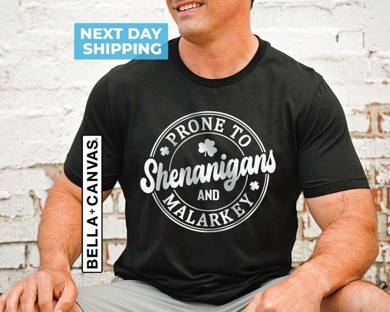 May include: Black t-shirt with a silver circle graphic that says "Prone to Shenanigans and Malarkey" with a shamrock design.