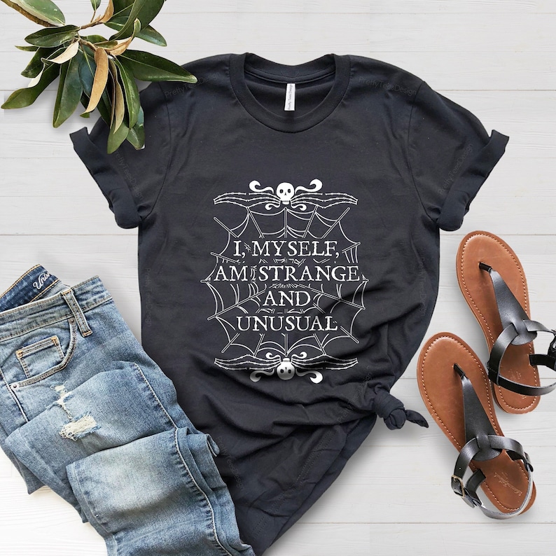 Op de afbeelding: Zwart T-shirt met een wit spinnenwebontwerp en de tekst "I, myself, am strange and unusual".