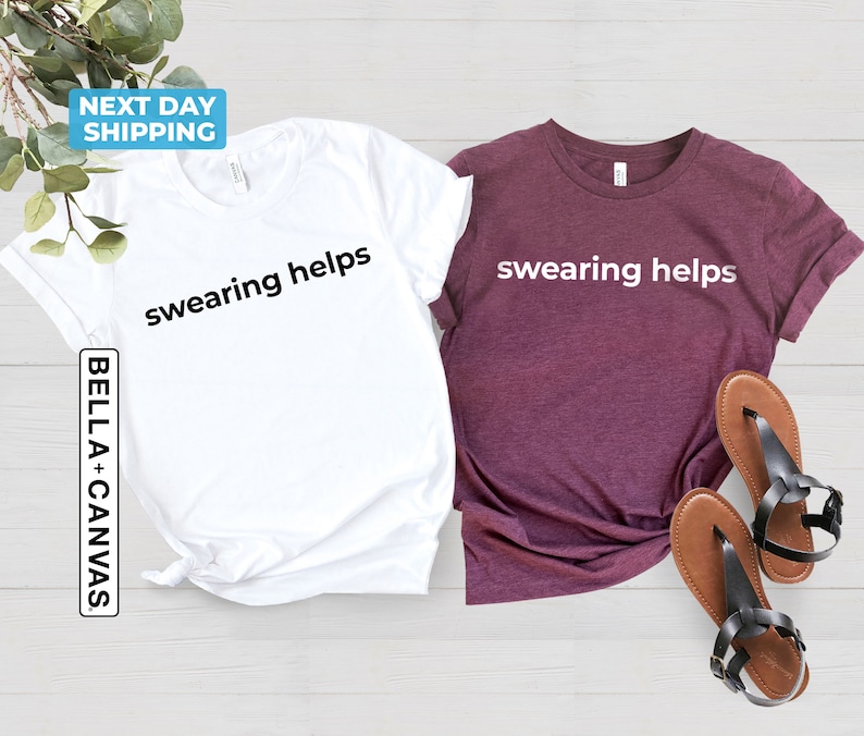 Op de afbeelding: Twee T-shirts met de tekst "swearing helps" erop gedrukt. E&eacute;n shirt is wit en de andere is bordeaux.