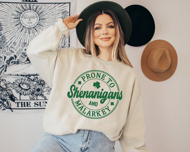 May include: A cream-coloured sweatshirt with a green circle graphic that says "Prone to Shenanigans and Malarkey" with a shamrock inside the circle.
