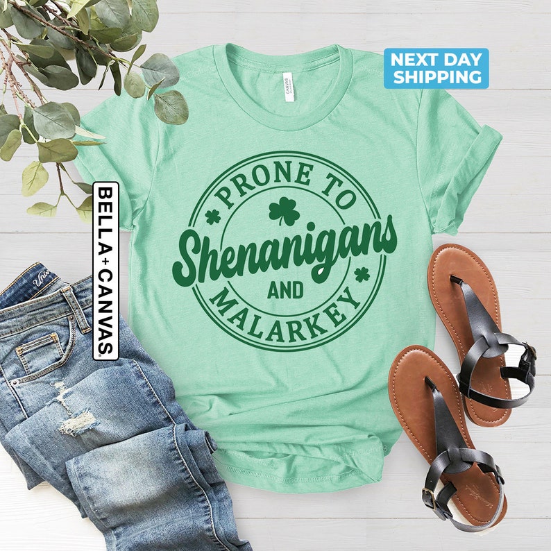May include: A light green t-shirt with a green circle graphic that says "Prone to Shenanigans and Malarkey" with shamrock designs.