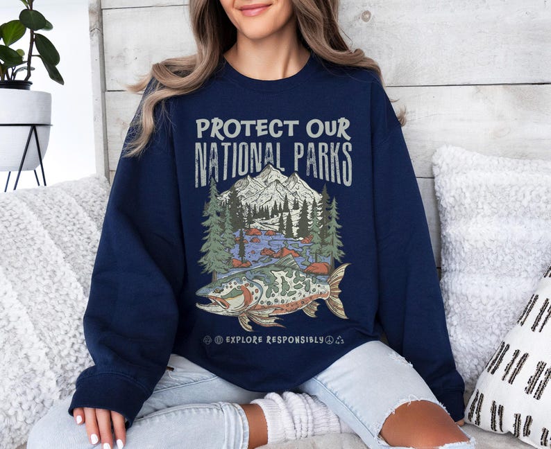 May include: Navy blue sweatshirt with a graphic that reads "PROTECT OUR NATIONAL PARKS." The graphic features a mountain range, trees, a river, and a fish. The text "EXPLORE RESPONSIBLY" is below the graphic.