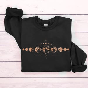 May include: Black sweatshirt with a graphic of a crescent moon and phases of the moon in a line with a star and other celestial symbols.