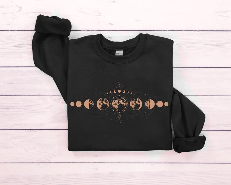 May include: Black sweatshirt with a graphic of a crescent moon and phases of the moon in a line with a star and other celestial symbols.