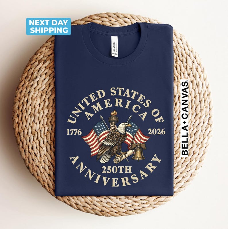 May include: Navy blue t-shirt featuring a patriotic design for the 250th anniversary of the United States. The design includes an eagle, American flags, and the text "United States of America 250th Anniversary".