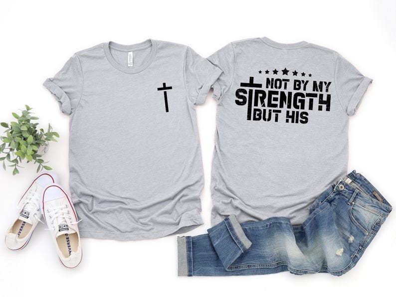 May include: A gray t-shirt with a cross on the front and the text "Not by my strength but his" on the back.