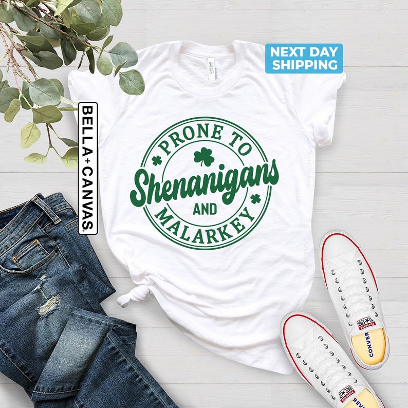 May include: White t-shirt with a green circle graphic that says "Prone to Shenanigans and Malarkey".