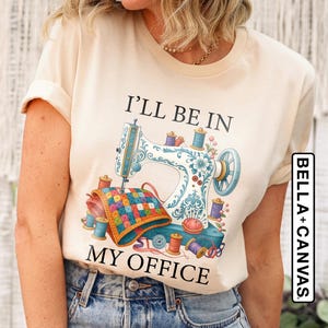 May include: Cream-colored t-shirt featuring a sewing machine design with the text "I'll Be In My Office." The design includes spools of thread, a quilt, and floral accents. The shirt is made of soft material.
