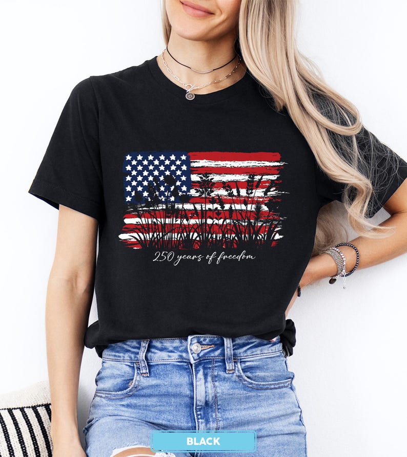 May include: Black t-shirt featuring a distressed American flag design with red and white stripes, blue stars, and wheat stalks. The text "250 years of freedom" is printed below the flag. The shirt is made of a soft material.