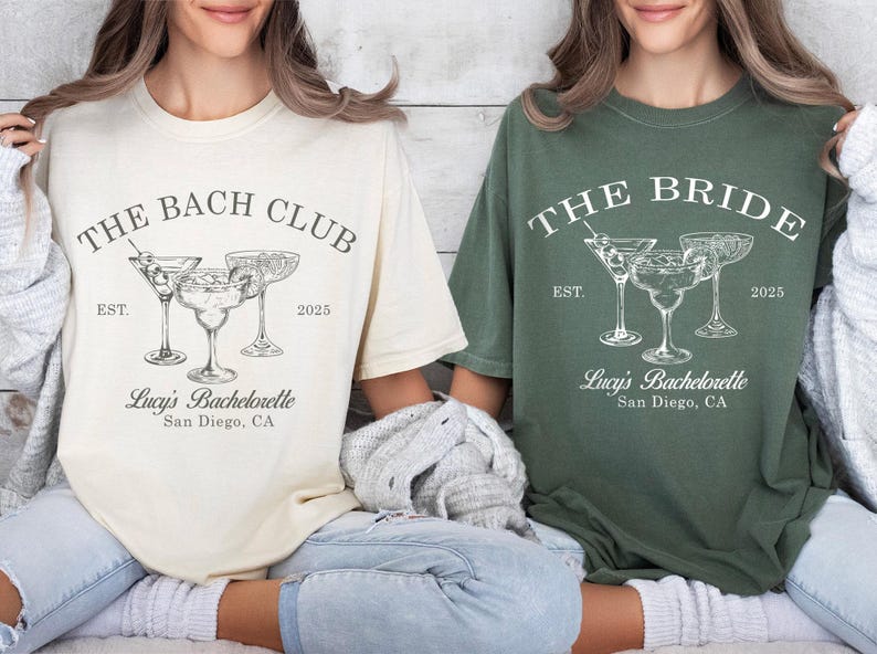 May include: Two white t-shirts with a bachelorette party theme. The text on the shirts reads "The Bach Club" and "The Bride". Both shirts feature a graphic of three cocktail glasses with olives and a text that reads "Lucy's Bachelorette, San Diego, CA".