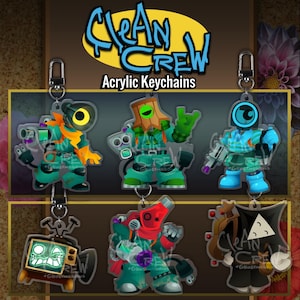 May include: Six acrylic keychains featuring stylised characters with vibrant colours, including a television head, a bucket head, and various robotic figures. The text Clean Crew Acrylic Keychains is displayed at the top. Each keychain has a metal clasp.