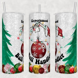 May include: A white tumbler with a lid and straw, featuring a Christmas theme. The design includes a skeleton hand holding Christmas lights and a red ornament with snowflakes. Text reads "Experienced Ball Handler". Green Christmas trees and ornaments decorate the sides.