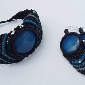 Peut inclure: Ensemble de bijoux en macramé comprenant un bracelet et des boucles d'oreilles. Le bracelet et les boucles d'oreilles présentent un motif en macramé noir avec des accents bleus et argentés. Chaque pièce comporte une grosse pierre ovale bleue.