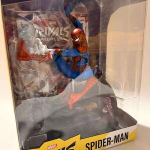 May include: A Spider-Man action figure in a clear plastic display case. The figure is in a dynamic pose, wearing a red and blue suit. The packaging includes the text "Marvel Rivals" and "Spider-Man". The box also says "Includes Comic Book" and "Gamer Verse".