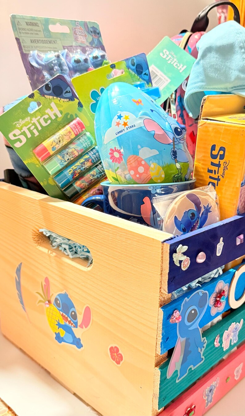 K&ouml;nnte beinhalten: Eine Holzkiste gef&uuml;llt mit Disney Stitch-Merchandise. Zu den Artikeln geh&ouml;ren Lippenbalsam, Figuren, ein Becher und ein eif&ouml;rmiger Beh&auml;lter. Die Kiste ist mit Stitch-Aufklebern und farbenfrohen bemalten Akzenten verziert.