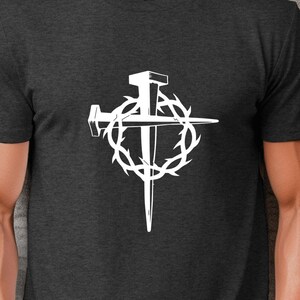 May include: A dark heather grey t-shirt with a white graphic of a cross with nails and a crown of thorns.