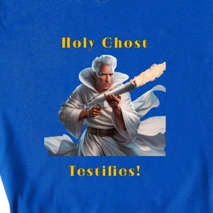 Puede incluir: Una camiseta de cuello en V azul real con una imagen blanca de un hombre con una túnica blanca sosteniendo un arma en llamas. El texto "Holy Ghost Testifies!" está impreso en amarillo en la camiseta.