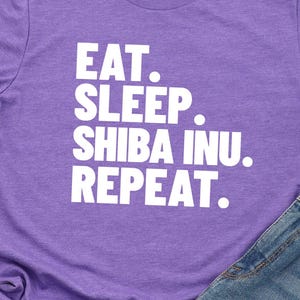 May include: Purple t-shirt with white text that reads "Eat. Sleep. Shiba Inu. Repeat."