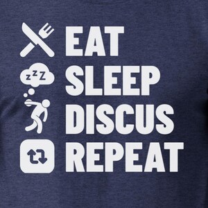 May include: A navy blue t-shirt with white text that reads "Eat Sleep Discuss Repeat". The text is arranged vertically with a fork and knife, a sleeping face, a stick figure throwing a disc, and a recycle symbol.