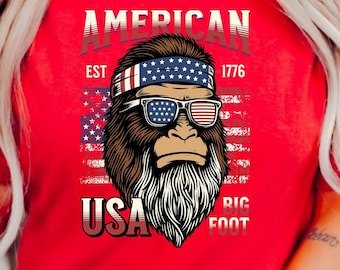 Puede incluir: Camiseta roja con un gráfico de Bigfoot con gafas de sol y una bandana con la bandera estadounidense. El texto "AMERICAN EST 1776 USA BIGFOOT" está impreso en la camiseta.
