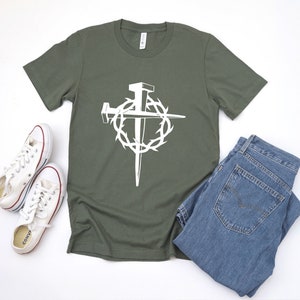 May include: A green t-shirt with a white graphic of a cross made of nails surrounded by a crown of thorns.