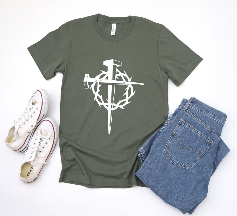 May include: A green t-shirt with a white graphic of a cross made of nails surrounded by a crown of thorns.