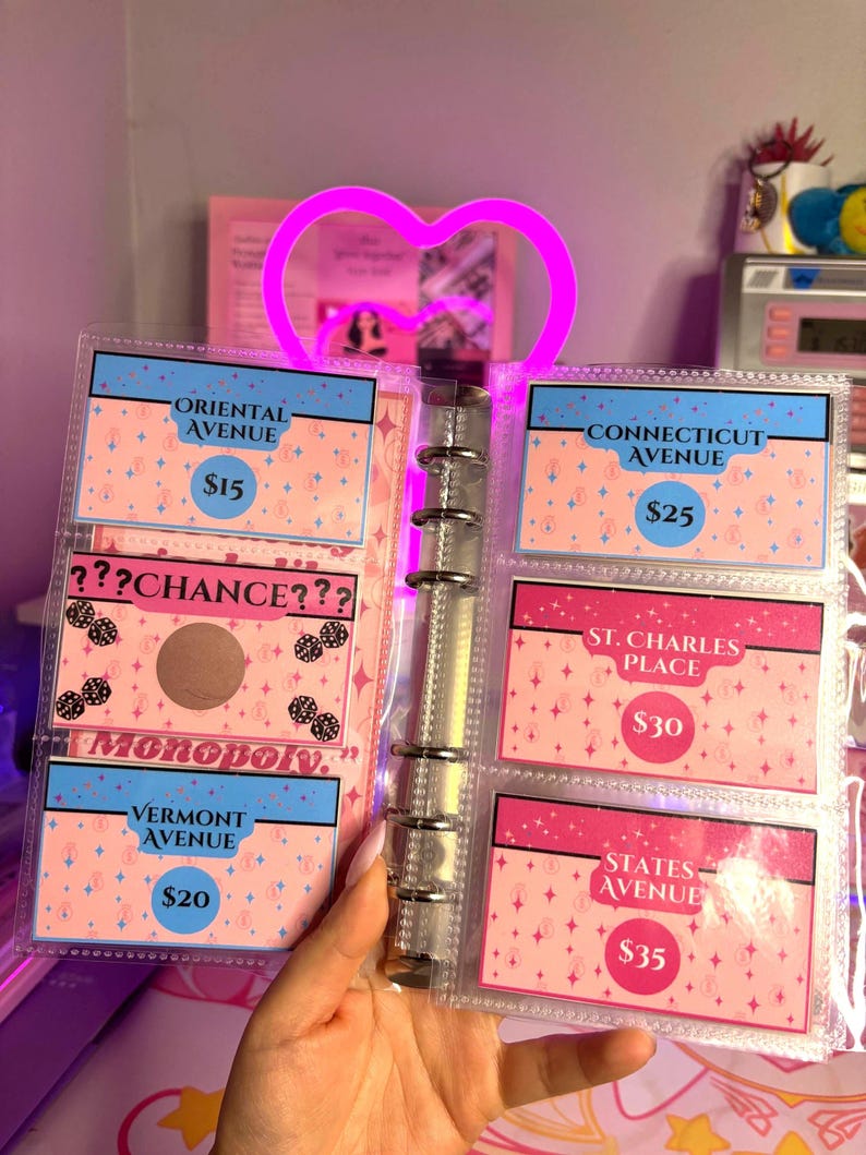 May include: A Monopoly-themed card holder with cards featuring property names like Oriental Avenue and Vermont Avenue. The cards are pink and blue with prices listed. The holder has a heart-shaped light.