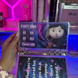May include: A clear plastic binder with a colorful page featuring a character from the movie "Coraline" and a quote about bravery. The page also includes a price list with the text "Part One" and prices for different items. The total price is $25.