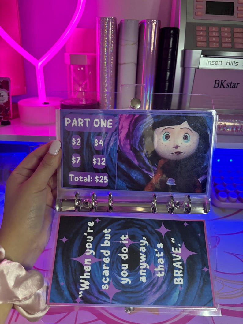 May include: A clear plastic binder with a colorful page featuring a character from the movie "Coraline" and a quote about bravery. The page also includes a price list with the text "Part One" and prices for different items. The total price is $25.