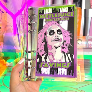 May include: A clear plastic binder with a colorful, illustrated page featuring a character from the movie Beetlejuice. The page has the text "Beetlejuice (Beetlejuice)" and "Savings".