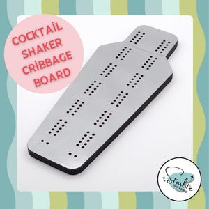 May include: A silver cribbage board with black edges and numerous holes for pegs. The board is shaped like a cocktail shaker and has the words "COCKTAIL SHAKER CRIBBAGE BOARD" in a pink circle. The Starlite Workshop logo is in the bottom right corner.