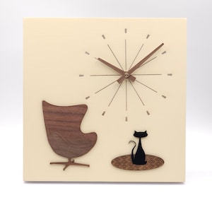 May include: A beige square clock with a brown wooden egg chair and a black cat silhouette on a brown rug. The clock face has a starburst design with brown hour and minute hands.