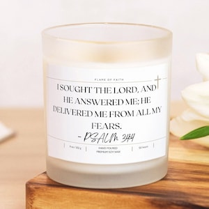 May include: White frosted glass candle jar with a black label. The label reads "FLAME OF FAITH" and a bible verse: "I sought the Lord, and he answered me; he delivered me from all my fears. - PSALM 34:4". The candle is hand-poured with premium soy wax and has a burn time of 50 hours.