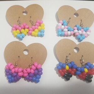 May include: Four pairs of heart-shaped earrings made from colorful beads. The earrings are attached to brown heart-shaped cardboard displays. The earrings feature various color combinations, including pink, yellow, blue, and white.