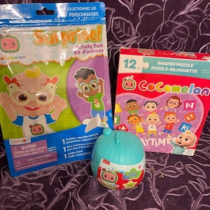 May include: A Cocomelon-themed activity pack with a 12-piece shaped puzzle, a sticker sheet, and a mini coloring book. The puzzle features characters from the show, including a baby wearing a blue shirt and a baby wearing a pink shirt. The sticker sheet has a variety of characters and objects from the show. The mini coloring book has a cover featuring a baby wearing a blue shirt. The packaging is pink and purple with the Cocomelon logo and the words "Shaped Puzzle" and "Puzzle-Silhouette".