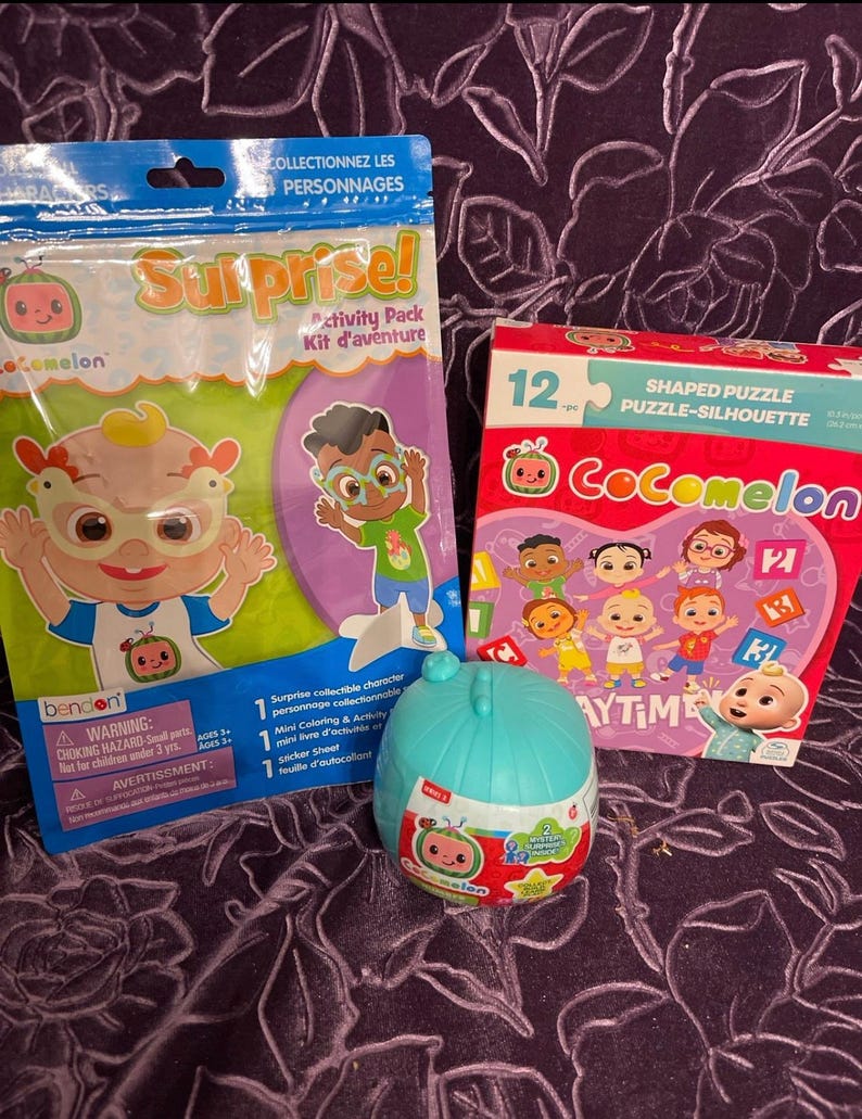 May include: A Cocomelon-themed activity pack with a 12-piece shaped puzzle, a sticker sheet, and a mini coloring book. The puzzle features characters from the show, including a baby wearing a blue shirt and a baby wearing a pink shirt. The sticker sheet has a variety of characters and objects from the show. The mini coloring book has a cover featuring a baby wearing a blue shirt. The packaging is pink and purple with the Cocomelon logo and the words "Shaped Puzzle" and "Puzzle-Silhouette".