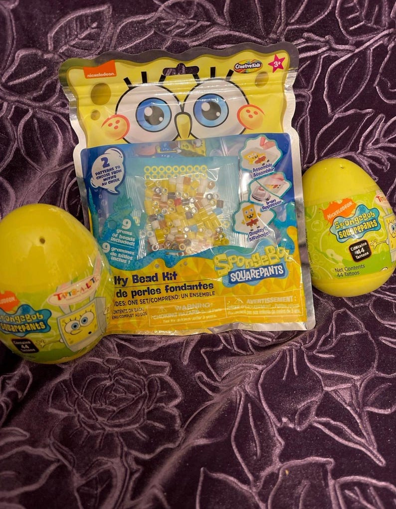 May include: A SpongeBob Squarepants themed bead kit with a yellow plastic egg containing 44 tattoos. The bead kit includes a variety of colorful beads, a bead board, and an iron-on design. The kit is packaged in a clear plastic bag with a SpongeBob Squarepants character on the front.